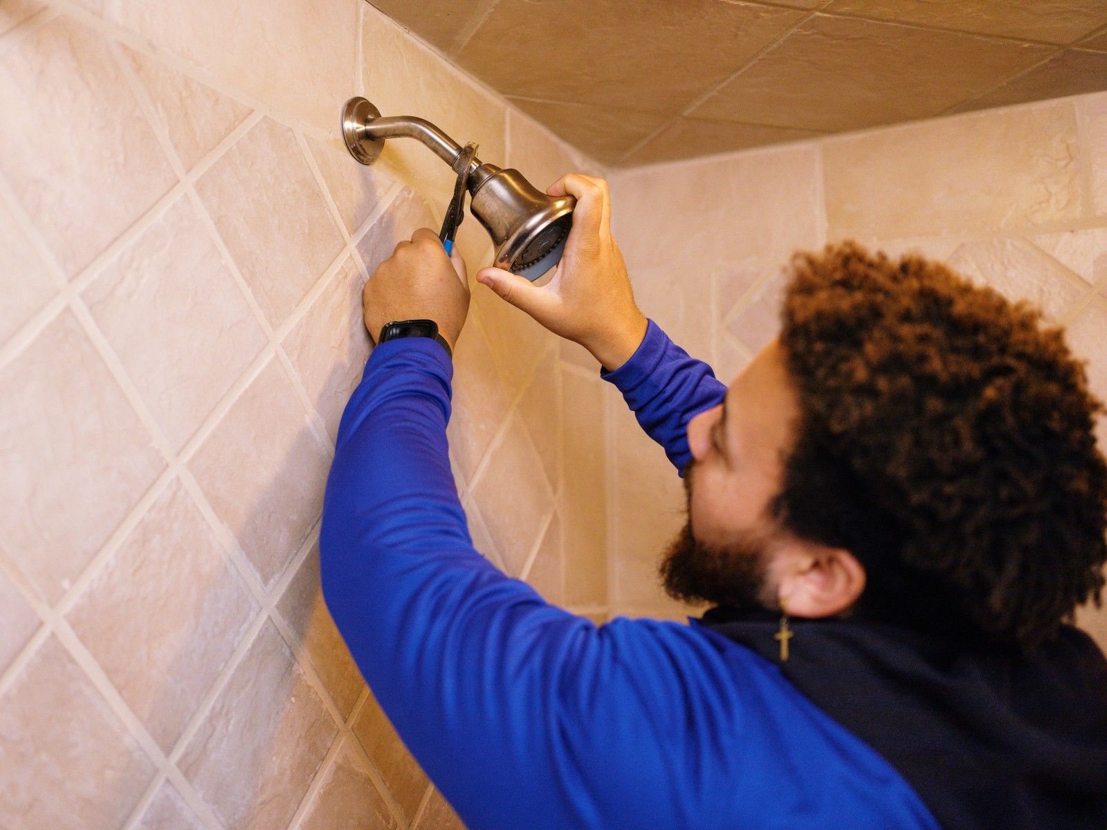 Plumber In Blue Uniform Repairing Showerhead With Wrench In Tiled Bathroom