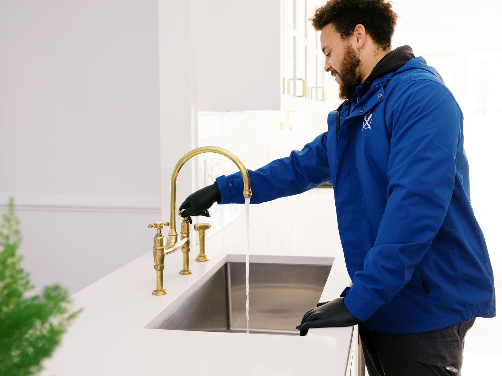 Plumber In Blue Uniform Testing Running Water From Brass Kitchen Faucet